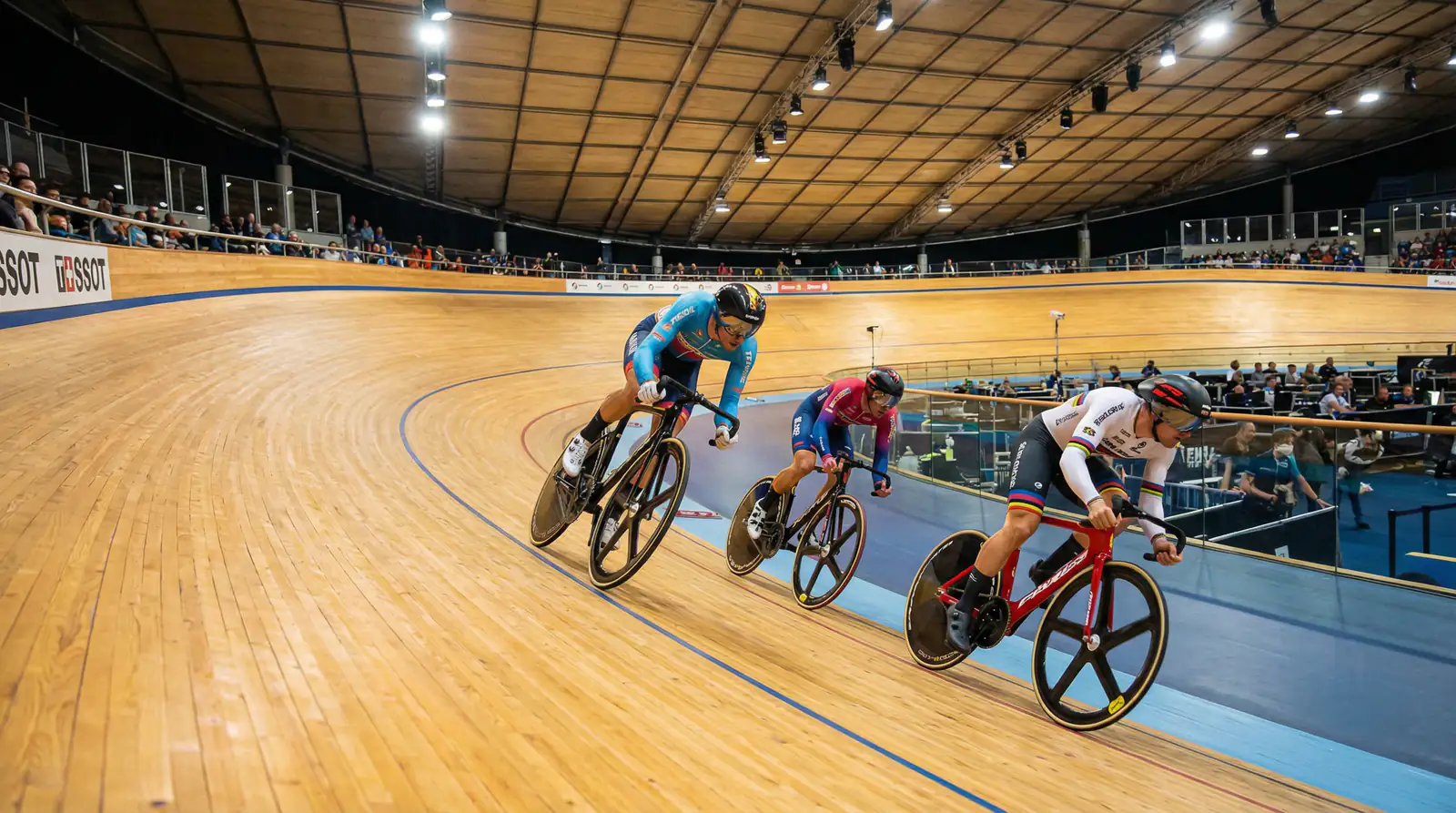 Ciclistas compitiendo en un velódromo de pista con las curvas peraltadas de madera visibles
